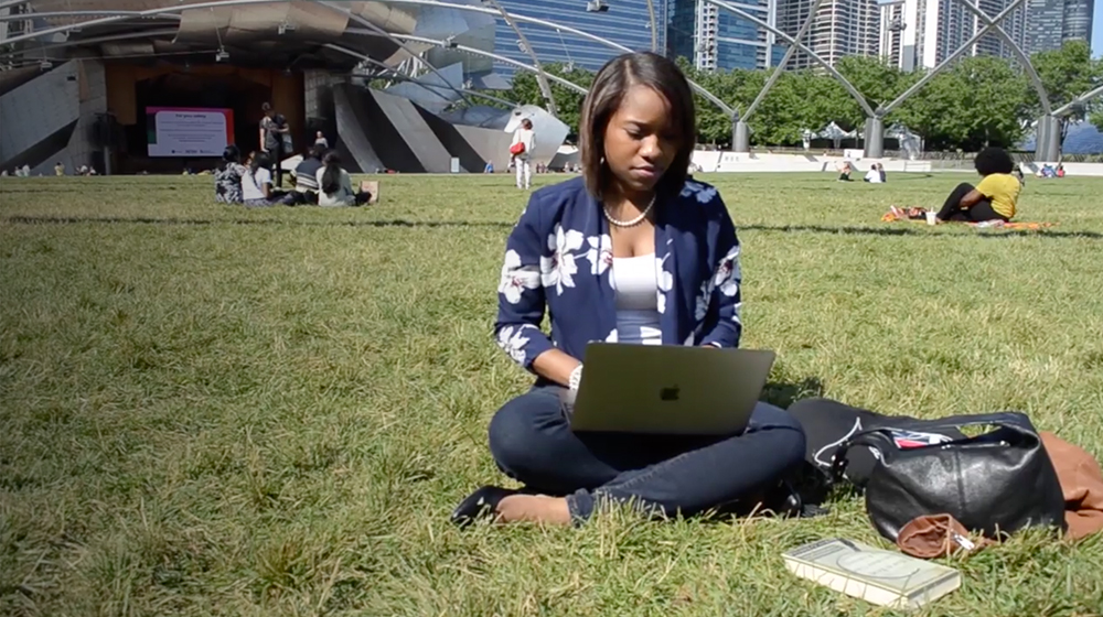 Ptahra Jeppe a law student sits in a park using her laptop.