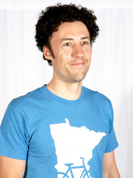 Kevin Johnston smiles off camera in front of white background wearing bright blue shirt