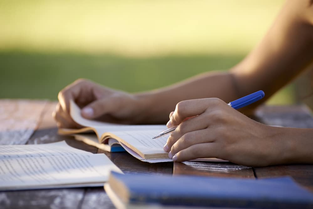Close up of a woman's hands studying outside with pen and paper