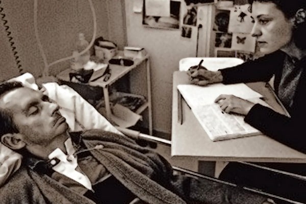 Man in a hospital bed with woman writing