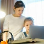 Mother helping her daughter as she uses laptop for eLearning